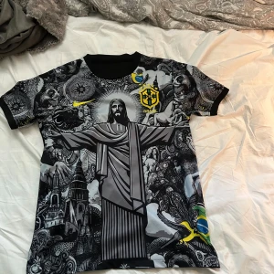 Brasil Nike fotbollströja grafisk svart - Unik Brasilien fotbollströja från Nike med grafiskt tryck av Kristusstatyn och brasilianska symboler. Svart och grå bas med gula detaljer, CBF-emblem och Nike-logga. Kortärmad modell i lätt, ventilerande material. Perfekt för dig som vill sticka ut på planen eller läktaren.
