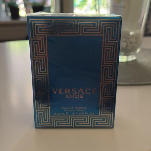 Versace Eros Eau de Parfum 100ml - Versace Eros Eau de Parfum 100ml i en snygg blå och guldig kartong med klassiskt grekiskt mönster. Lyxig och ikonisk doft från Versace, perfekt för dig som vill sticka ut. Flaskan är försluten i originalförpackning och tillverkad i Italien.