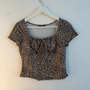 Leopardmönstrad topp  - Snygg leopardmönstrad topp från SHEIN med korta ärmar och rundad urringning. Toppen har en söt knytning framtill och är figurnära i modellen. Perfekt för dig som vill sticka ut med ett djurmönster och gillar trendiga detaljer. Storlek S