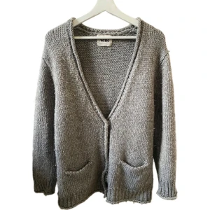 Grå stickad kofta från Acne Studios  - Snygg grå stickad kofta från Acne med v-ringning, knappar framtill och två fickor. Koftan är gjord i ett tjockare garn, som är en blandning av merinoull, akryl och alpacka, och är därav lite nopprig. Köpt för 2150kr på Vestiaire Collective.