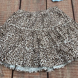 Leopardmönstrad volangkjol från SHEIN - Kort kjol från SHEIN med leopardmönster i brunt, svart och beige. Kjolen har flera volanger och resår i midjan för en bekväm passform. Perfekt för dig som vill sticka ut med en trendig och lekfull stil.
