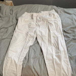 Randiga linnebyxor från 157, storlek S - Snygga och lätta linnebyxor från 157 i beige och vitt med smala ränder. Byxorna har resår i midjan för extra komfort och en avslappnad passform. Perfekta för varma dagar när du vill ha en chill och stilren look.