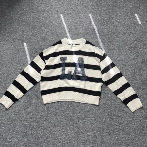 Randig stickad tröja LA H&M - Snygg stickad tröja från H&M med breda svarta och vita ränder och stort LA-tryck framtill. Modellen är croppad med ribbade muddar och rund hals. Perfekt för dig som  gillar streetstyle och vill sticka ut lite extra.