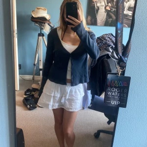 Mörkblå ribbad kofta med knappar - Säljer en mörkblå kofta med ribbad struktur och v-ringning från Brandymelville. Koftan har långa ärmar och stängs med små knappar framtill. Perfekt att slänga över ett linne eller topp eller även bara bikini. Materialet känns mjukt och stretchigt.