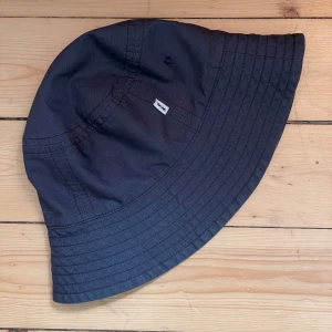 Mörkblå bucket hat från Wood Wood - Mörkblå bucket hat från Wood Wood med bredare brätte och diskret logga på sidan. Ofodrad i bomull. Inköpt på sample sale.