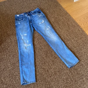Ljusblåa unika Replay jeans med slitningar - Säljer ett par blå Replay jeans med snygga slitningar perfekt inför vår och sommar. Köpta i somras på NK Göteborg men tyckte inte att de passat mig så används endast en gång, tags medföljer, jeansen är helt nya. Nypris:2000 