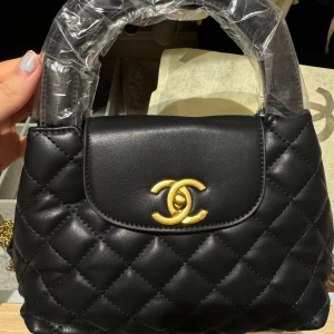 Snygg och lyxig svart väska  - Elegant svart quiltad handväska med gulddetaljer och kedja. Väskan har ett klassiskt märke på framsidan och en praktisk handrem. Perfekt för att ge en lyxig touch till din outfit. Väskan är ny och oanvänd! Skriv till mig för flera bilder. Kedja ingår (köptes för 1500kr) 