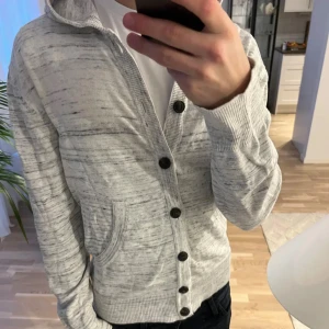 Cardigan med knappar - Riktigt snygg gråvit cardigan med svarta knappar! Strl L men sitter som M