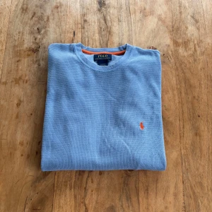 Polo Ralph Lauren – Ljusblå långärmad tröja i strukturstickat tyg - Avslappnad och snygg tröja i ljusblått strukturstickat tyg med broderad logga i rött och kontrastfärgad insida vid kragen.  Storlek: M (normal i storlek) Färg: Ljusblå med röd logga Material: 60% bomull, 40% polyester Skick: Mycket fint skick – inga hål eller fläckar Stil: Casual / Preppy / Vintage Passform: Rak modell med rund hals och ribbade muddar Nypris: ca 1 000 kr Pris: 290 kr  Frakt: Skickas snabbt & spårbart 