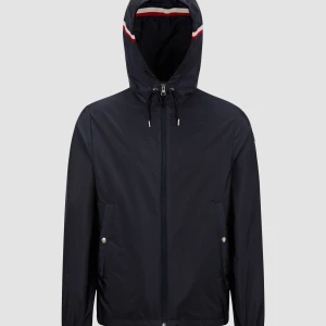Moncler Windbreaker - Snygg svart vindjacka från Moncler med huva och dragkedja framtill. Jackan har Moncler-logga på ärmen och rödvit randdetalj på huvan. Perfekt för blåsiga dagar och enkel att matcha med det mesta.