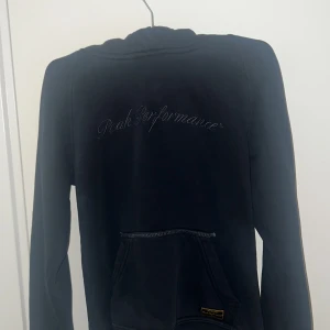 Svart hoodie från Peak Performance - Mörkblå eller svart hoodie från Peak Performance med broderad logga på bröstet och magficka framtill. Klassisk huva och mjukt material, perfekt för en avslappnad stil. Strl S men sitter som XS