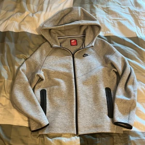 Grå hoodie från Nike - Säljer en Nike tech ny modell för 400 kr. Storleken är XL i barn och XS i herr. Passar perfekt till dig som är mellan 160 till 170 cm lång. 