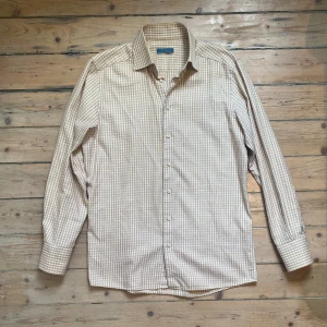 Beige och vit rutig skjorta från Eton XL - Säljer en klassisk långärmad skjorta från Eton i beige och vitt rutigt mönster. Skjortan har knappar framtill och på ärmsluten, samt en mjuk krage. Perfekt för dig som gillar stilrena och tidlösa plagg. 