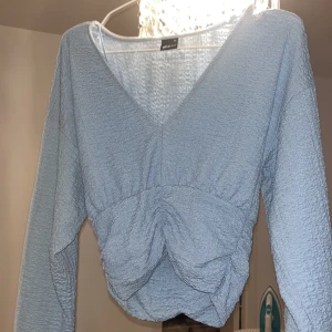 Ljusblå v-ringad topp med rynkade detaljer -  ljusblå långärmad topp/blus från Gina tricot med v-ringning och rynkade detaljer framtill. 