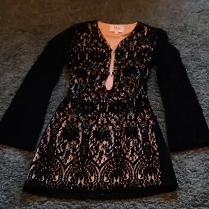 Svart spetsklänning med lång ärm från Eton - Supersnygg svart spetsklänning från Eton med lång ärm och v-ringning. Klänningen har ett vackert blommigt spetsmönster och en liten öppning framtill. Perfekt för dig som vill sticka ut med elegans.