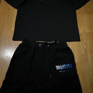 Svarta shorts från Trapstar med broderad logga - Svarta shorts från Trapstar med broderad logga i vitt, ljusblått och blått på vänster ben. Shortsen har snörning i midjan och är tillverkade i mjuk bomull. Perfekta för en avslappnad streetwear-look.