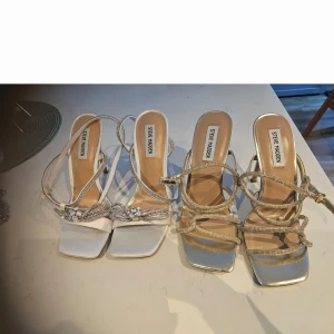 Steve Madden sandaler med klack och glittriga detaljer - Säljer ett par snygga sandaler från Steve Madden med fyrkantig tå, klack och glittriga remmar. Skorna har öppen tå och dekorativa stenar framtill. Använd en gång.  Ny  pris 1395 kr Perfekta för att lyfta din outfit med lite extra bling på bal,bröllop, fest. 650 kr per st