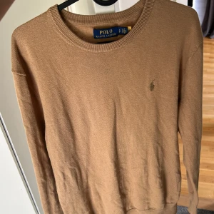 Beige stickad tröja från Polo Ralph Lauren - Säljer en klassisk beige stickad tröja från Polo Ralph Lauren. Tröjan har rund halsringning, långa ärmar och den ikoniska broderade loggan på bröstet. Perfekt för en stilren och avslappnad look.