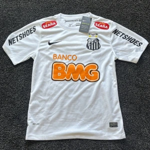 Vit Santos Neymar Jr 11 fotbollströja - Säljer en vit Santos fotbollströja från Nike med Neymar Jr och nummer 11 på ryggen. Tröjan är aldrig använd och den är helt ny med taggar kvar. Jag säljer tröjan pga att den inte har kommit till användning.