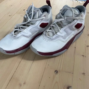 Jordan Stay Loyal 3 vita och röda basketskor - Säljer ett par Jordan Stay Loyal 3 sneakers i vitt med röda detaljer och logga. Skorna har snörning, rund tå och platt sula. Perfekta för dig som gillar sportig stil och vill ha något bekvämt till vardags. Skorna är lite slitna undertill eftersom de är använda som basketskor utomhus ca 2-3 veckor men sedan bara använda inomhus. Det finns en liten röd fläck (vet inte vad det är) på plösen men syns inte medans de används. 