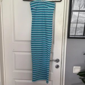 Randig tubklänning i blått och vitt - Säljer en tubklänning med blå, turkosa och vita ränder. Klänningen är lång och har en tight passform. Perfekt för sommardagar och enkel att styla med sneakers eller sandaler. Materialet är mjukt och stretchigt för en bekväm känsla. Klänningen är aldrig använd💞