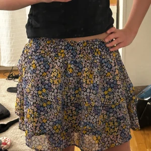 Blommig kortkjol från H&M - Säljer en söt blommig kortkjol från H&M med svart botten och blommor i blått, gult, lila och vitt. Använd fåtal gånger och säljer pga inte min stil längre!❤️Resår i midjan vilket gör så kjolen ger en skön passform(jag är 162cm och man ser ju hur kort kjolen är på mig!)🫶🏻
