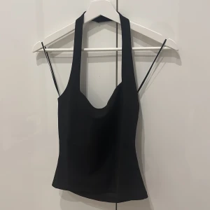 Svart halterneck topp - Snygg svart halterneck topp med djup urringning och smala band i ryggen. Toppen har en croppad passform och är perfekt för att skapa en trendig look. Tillverkad i ett mjukt och stretchigt material.