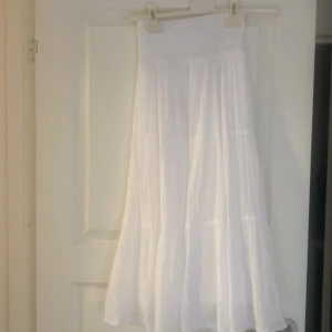 Vit långkjol med resår i midjan - Säljer en luftig och flowy vit långkjol med bred resår i midjan. Kjolen har flera volanger och är tillverkad i ett tunt, lätt material som passar perfekt till varma dagar. Enkel att matcha med olika toppar för en fräsch sommarlook.