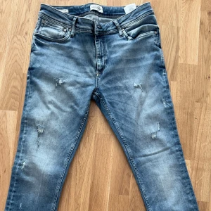 Blå slitna jeans från Jack & Jones - Säljer ett par blå jeans från Jack & Jones med slitna detaljer och klassisk femficksdesign. Jeansen har normal passform och är tillverkade i denim med lätt stretch. Perfekta för en avslappnad stil.