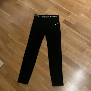 Svarta tights från Nike Pro - Svarta tights från Nike Pro med logga på midjan och ett litet vitt Nike-märke på benet. De har en tight passform och är perfekta för träning. Materialet är stretchigt och bekvämt. 