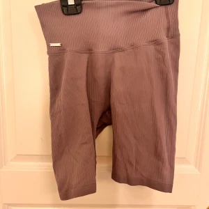 Lila ribbade cykelshorts från Aim'n - Säljer ett par lila cykelshorts från Aim'n med ribbad struktur och hög midja. Shortsen har en tight passform och är perfekta för träning eller en aktiv vardag. Mjukt och stretchigt material som sitter skönt på kroppen.