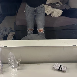 Grå slitna jeans från Zara - Säljer ett par grå jeans från Zara med snygga slitningar vid knäna. Jeansen har klassisk femficksdesign, dragkedja och knapp framtill. Modellen är rak och midjan är normal. Perfekta till en avslappnad stil.