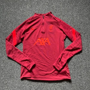 Liverpool tracksuit tröja - Säljer en vinröd tracksuit top från Nike i samarbete med Liverpool FC. Tröjan har halv dragkedja framtill. Storlek XL i barn men sitter som S/Small. Den är i bra skick och oerfekt för fotbollsträning och vardaglig användning. Hör av er vid frågor eller funderingar!