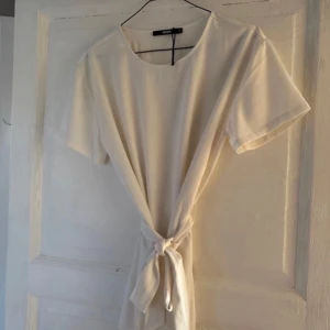 Vit t-shirt med knyt framtill - Säljer en stilren vit t-shirt med rund halsringning och korta ärmar. Toppen har en snygg knytdetalj framtill som ger en trendig look. Perfekt att matcha med jeans eller kjol för en enkel men snygg outfit.