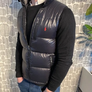 Ralph Lauren dunväst  - Säljer en blank svart Ralph Lauren dunväst i schysst skick! Inga hål eller liknade. På bild 3 ser man den enda defekten på västen, en ögla är trasig! Tänker mig runt 1200. Skriv om du har några frågor 😊