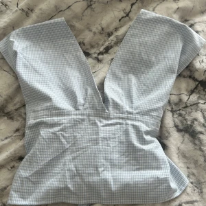 Rutig blus - Säljer en ljusblå och vit rutig blus med djup v-ringning och korta ärmar. Blusen har figurnära passform och är tillverkad i bomull. Perfekt för vår och sommar! Har sytt blusen själv så var försiktig när den tvättas då vissa sömmar kan spricka enkelt i tvättmaskin. Blusen har öppen rygg🩷