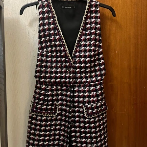 Rutig väst från Zara Basic - Säljer en snygg rutig väst från Zara Basic i färgerna svart, vit och röd. V-ringad modell med dekorativa guldkanter och två fickor framtill. Perfekt för att lyfta din outfit med en trendig touch.