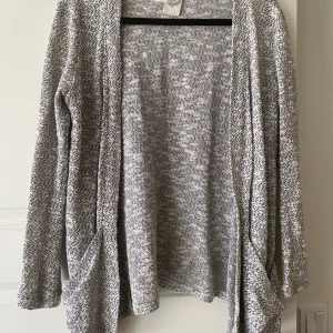 Gråmelerad stickad kofta från Zara - Mysig och lätt gråmelerad stickad kofta från Zara. Öppen framtill utan knäppning, med långa ärmar och avslappnad passform. Perfekt att slänga på sig över en t-shirt eller topp.