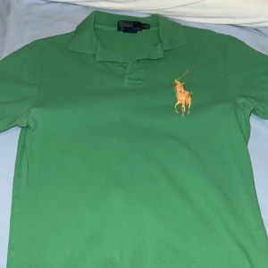 Grön pikétröja från Polo Ralph Lauren - Snygg grön pikétröja från Polo Ralph Lauren med klassisk krage och stor gul broderad logga på bröstet. Perfekt för sommaren och ren look