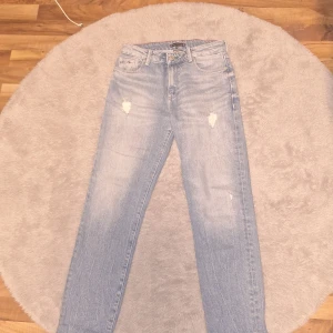 Ljusblå jeans från Tommy Hilfiger - Säljer ett par ljusblå jeans från Tommy Hilfiger med raka ben och slitna detaljer framtill. Klassisk femficksmodell med logga på bakfickan och patch i midjan. Perfekta för en avslappnad stil.