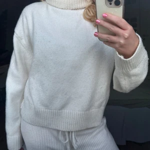 Vit stickad polotröja - Mysig vit stickad polotröja med bred ribbad mudd vid ärmslut och nederkant. Tröjan har en hög polokrage och en avslappnad passform, perfekt för kyliga dagar. Enkel och stilren design som passar till det mesta.