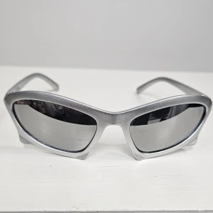 Silvriga cat eye-solglasögon - Snygga solglasögon i futuristisk cat eye-modell med silvrigt båge och mörka linser. Ramen är i plast och har en cool, modern vibe som sticker ut. Perfekt accessoar för dig som vill ha en edgy look.