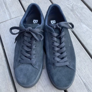 Mörkgrå sneakers från BOSS i mocka - Säljer ett par stilrena mörkgrå sneakers från BOSS i mjuk mocka. Skorna har rund tå, platt sula och klassisk snörning. Perfekta för dig som gillar en clean och tidlös look.