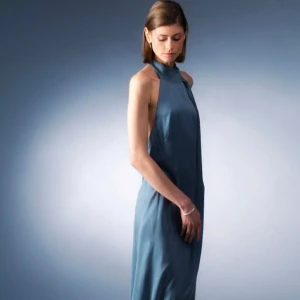 Blå långklänning med öppen rygg från Viela - Säljer en elegant blå långklänning med öppen rygg och knyt vid nacken. Klänningen har en slank siluett och är ärmlös, perfekt för speciella tillfällen. Materialet har en mjuk och följsam känsla. Klänningen är från Viela och är aldrig använd!!