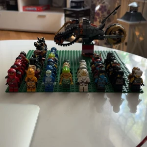 Instresskoll LEGO Ninjago minifigurer och fordon - Stor samling LEGO Ninjago minifigurer i olika färger och stilar, inklusive karaktärer med röda, gula, blå, vita, svarta och gröna dräkter. Flera figurer har detaljerade tryck, masker och tillbehör. Ett stort fordon med hjul och vapen ingår, allt monterat på gröna LEGO-plattor. INTRESSEKOLL!!!!!!!!