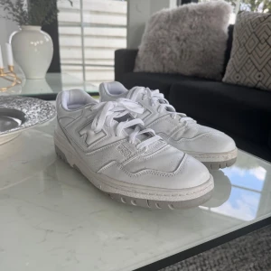 Vita New Balance 550 sneakers - Säljer ett par klassiska vita New Balance 550 sneakers med snygg retrodesign. Skorna har snörning, rund tå och platt sula. Perfekta för dig som gillar stilrena och sportiga sneakers.