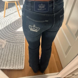 Victoria Beckham jeans - Säljer ett par mörkblå jeansbyxor från Victoria beckham med snygg broderad krona på bakfickan och lapp i midjan. Byxorna har bootcut-modell och ganska så lågmidjade.Perfekta för dig som gillar detaljer och en tidlös jeanslook.