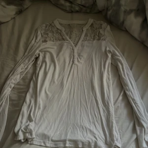 Vit långärmad topp med spetsdetaljer - Säljer en vit långärmad topp med v-ringning och knappar framtill. Storlek S men passar M också. Fina spets detaljer runt om tröjan. Är som ny.