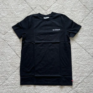 Svart t-shirt från Han Kjøbenhavn - Svart t-shirt från Han Kjøbenhavn med liten vit logga på bröstet. Klassisk rund halsringning och korta ärmar. Tillverkad i mjuk bomull och har en liten dansk flaggdetalj vid nederkanten.