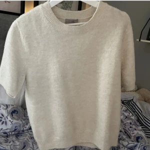 Vit stickad kortärmad tröja - Mysig vit stickad tröja med korta ärmar och rund halsringning. Perfekt för lager-på-lager eller som en enkel bas till din outfit. Mjuk och skön känsla.